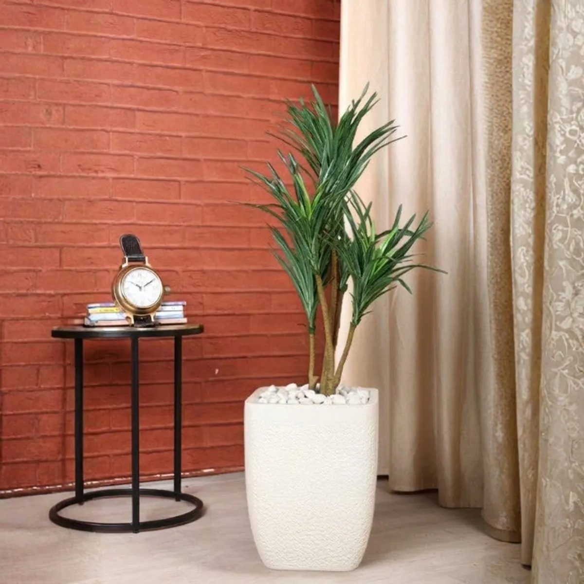 White floor planter with a green plant against a red brick wall