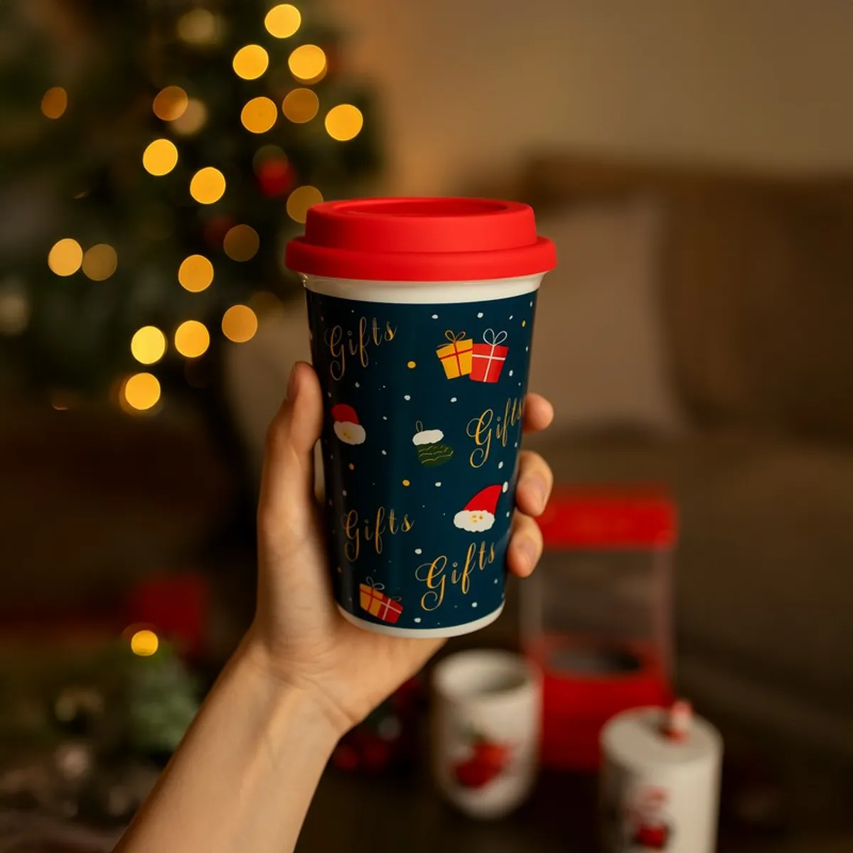 Hand holding a blue festive coffee mug with a red lid