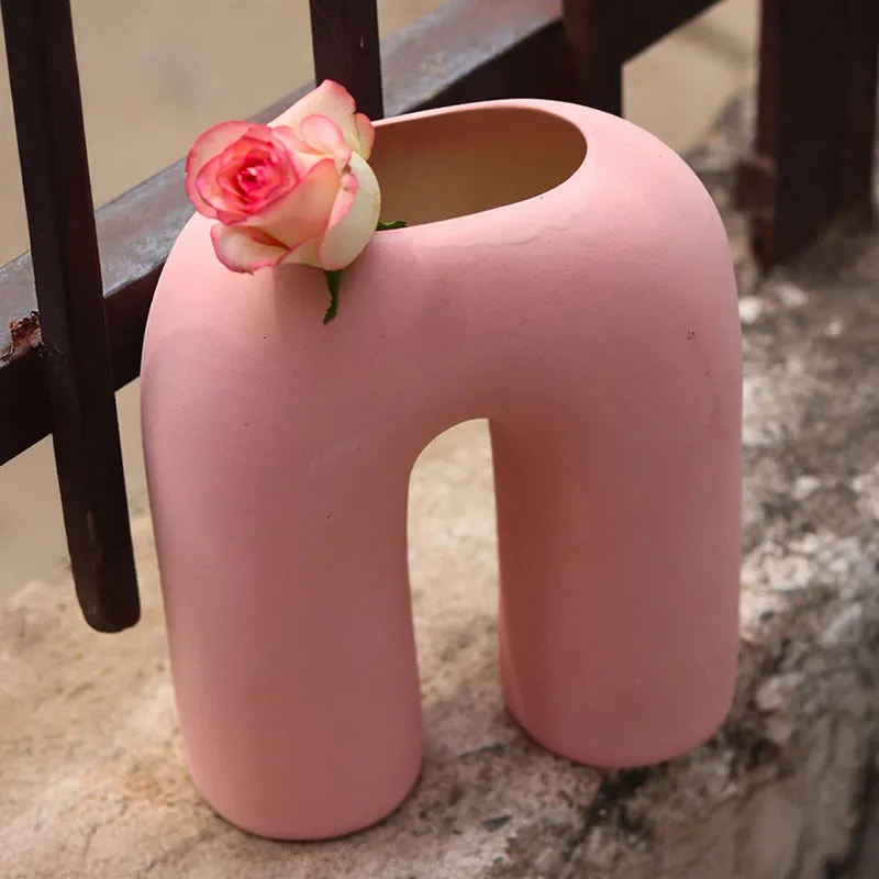 Angled view of a pink ceramic arc vase with a rose