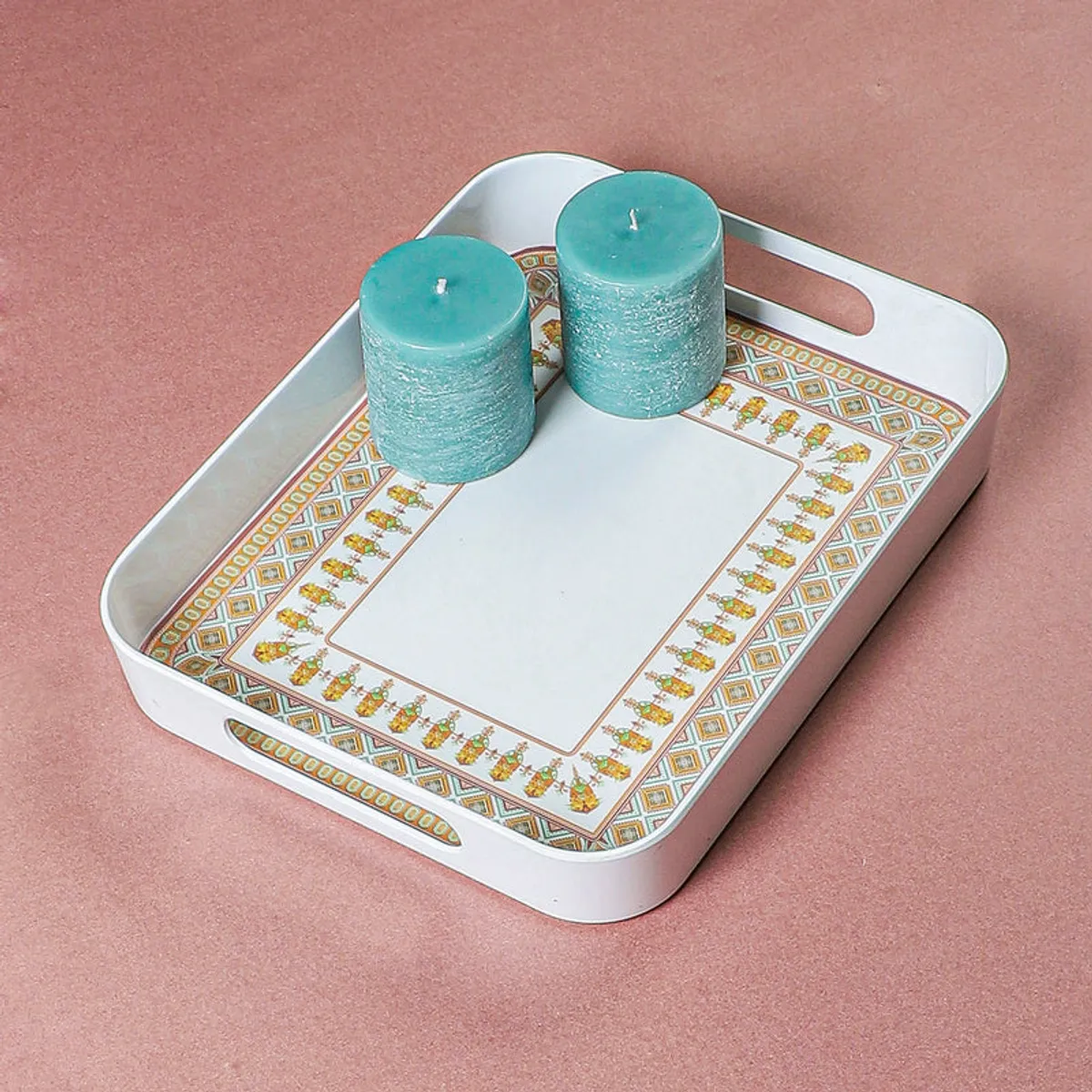 White serving tray with patterned border holding two turquoise candles