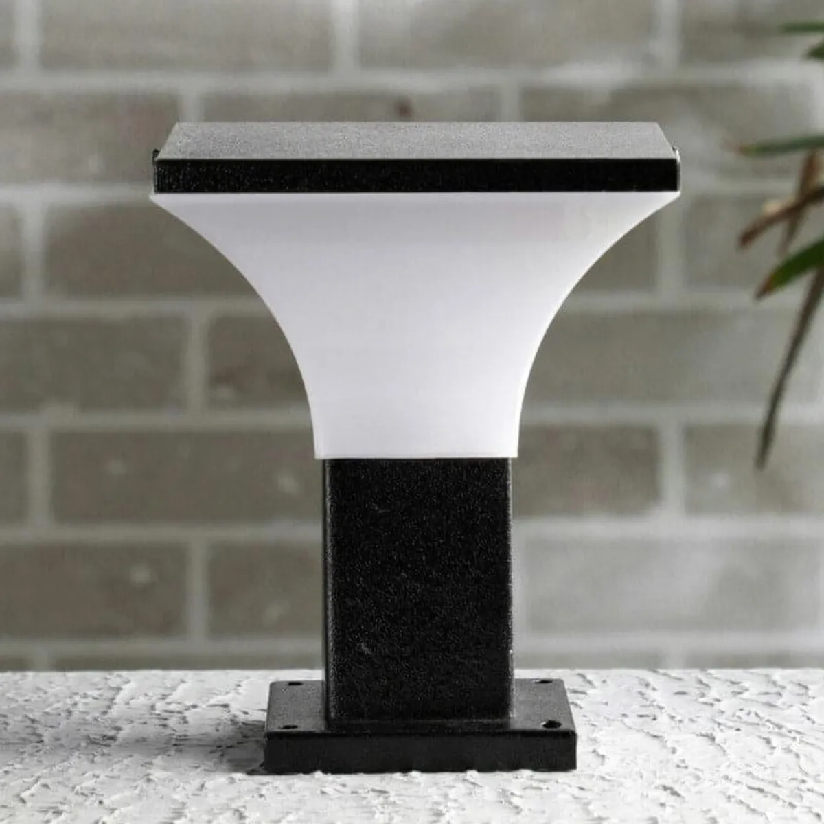 Black outdoor gate lamp with a white flared shade on a stone ledge