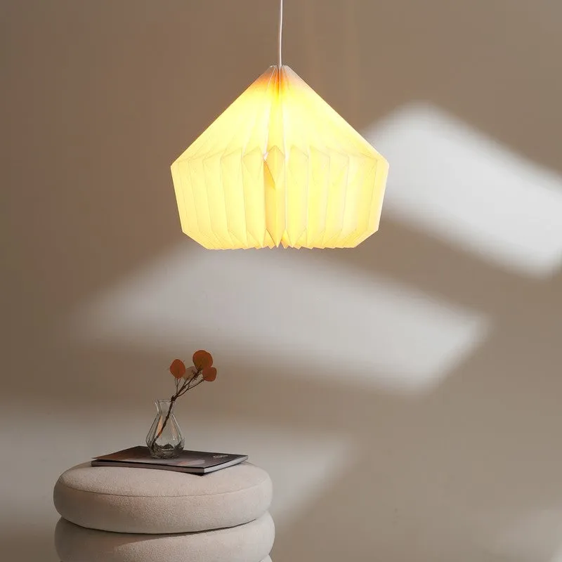 Bright folded pendant lamp above a low stool with a book and small vase