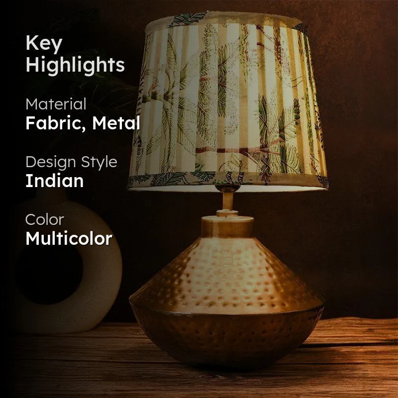 Lit table lamp with botanical shade and hammered gold-toned base in a styled setting
