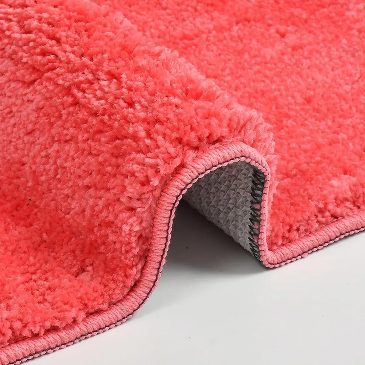Corner of the pink bath mat lifted to show its rubber bottom