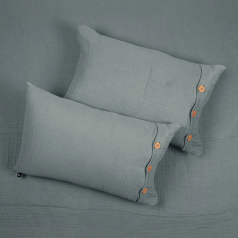 Two grey pillow covers with wooden buttons resting on the matching bedsheet