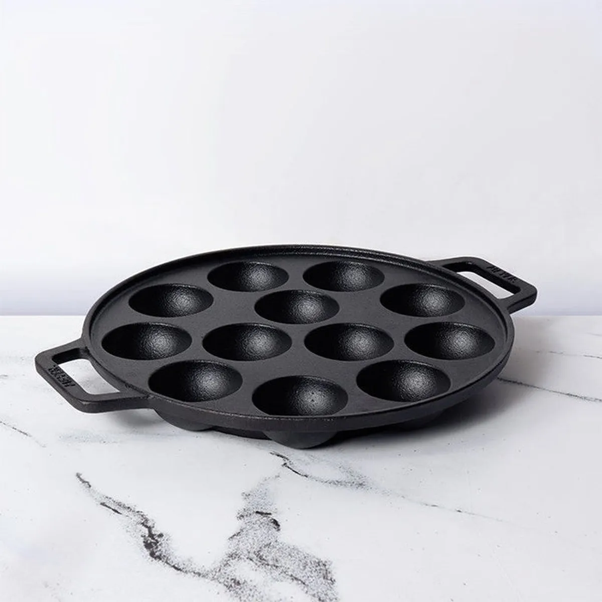Black round cast iron paniyaram pan shown on a white surface