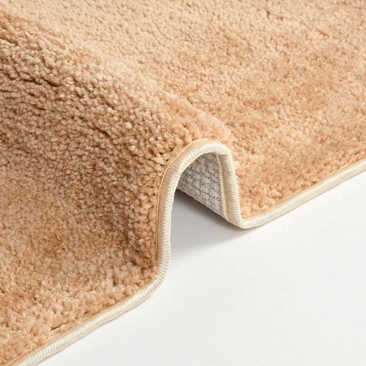 Close-up of the beige bath mat's bound edge and textured surface