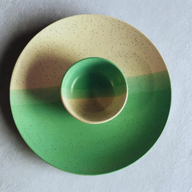Top view of a green and beige speckled plate with a bowl centred on it