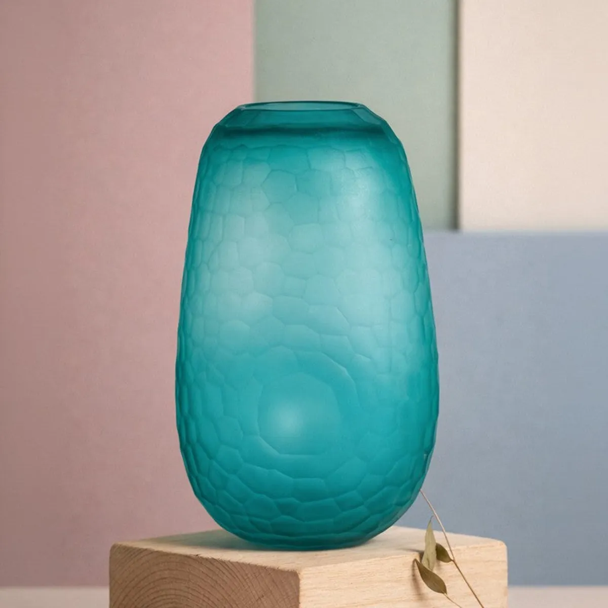Blue oval glass vase placed on a wooden block against a pastel backdrop