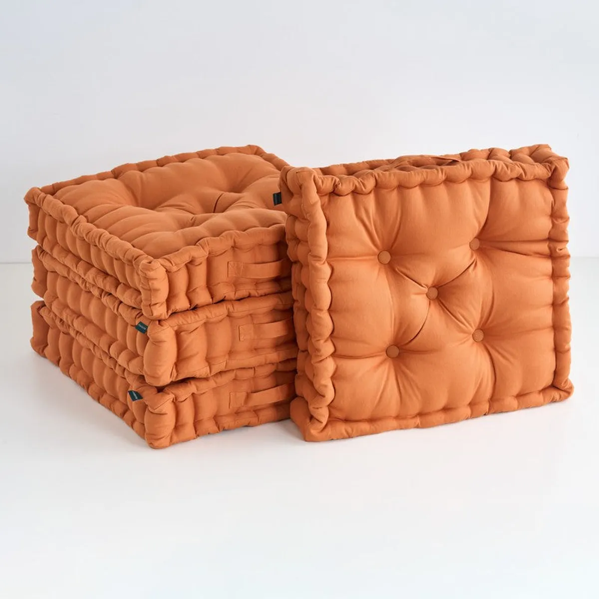 Stack of four brown tufted square floor cushions
