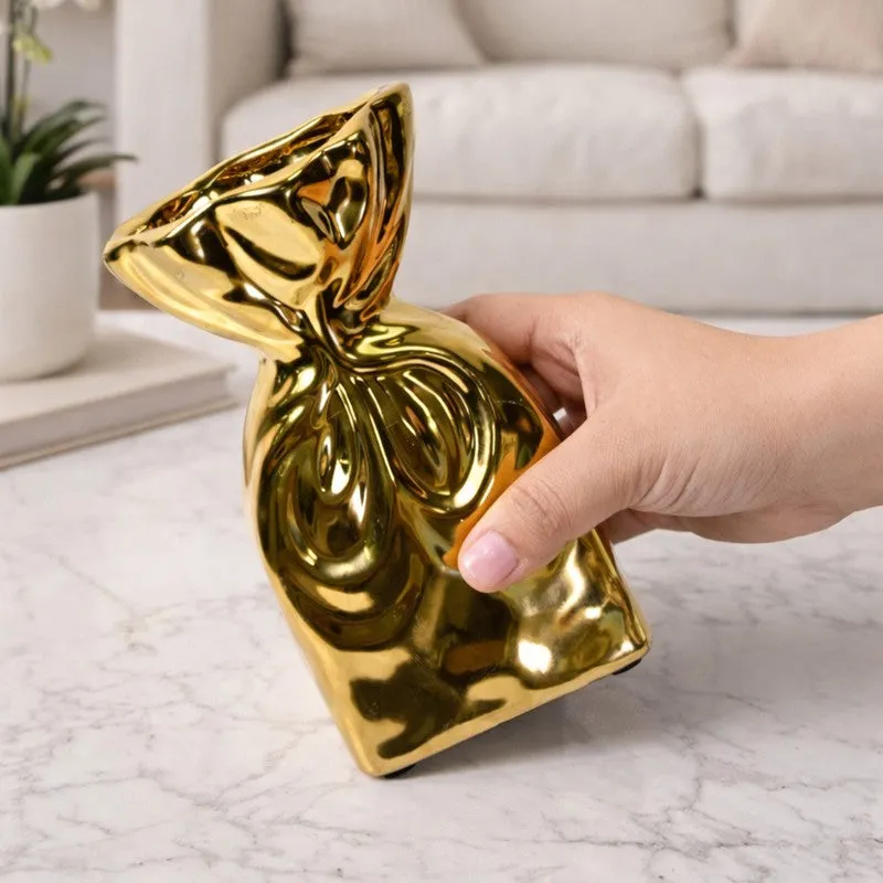 Hand holding a glossy gold sculptural vase over a marble surface