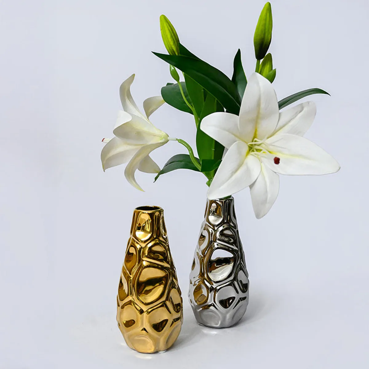 Gold and silver vases styled with white lilies against a plain background