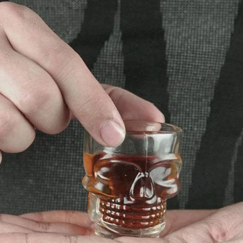 Hand holding a clear skull-shaped shot glass filled with a dark drink
