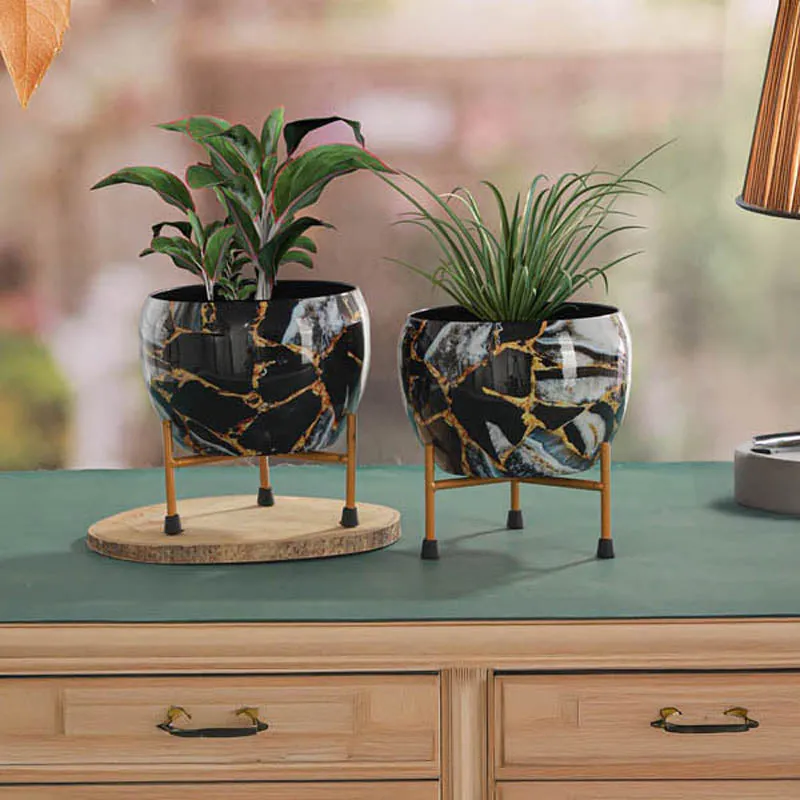 Two black marbled planters with gold veining on matching stands placed on a tabletop