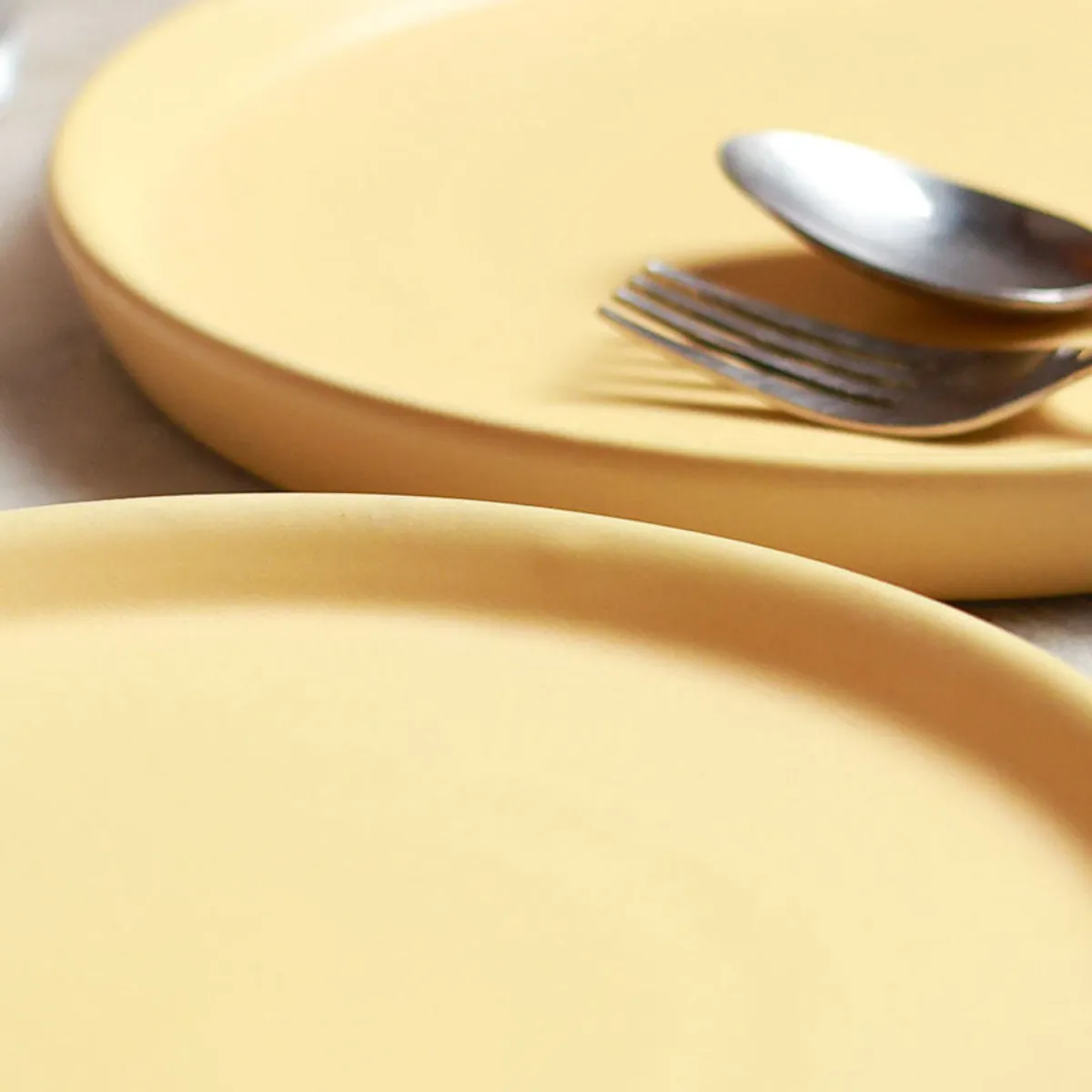Close-up of smooth yellow ceramic plates with cutlery
