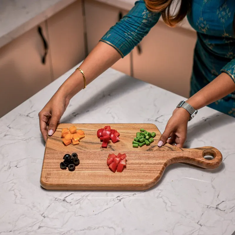 Person holding a brown wooden chopping board with chopped vegetables