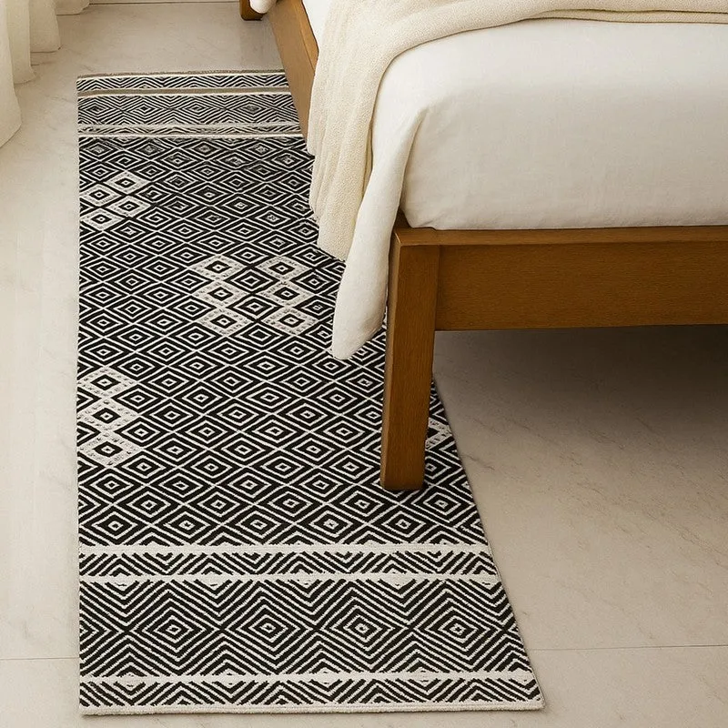 Black and off-white geometric runner rug placed beside a bed