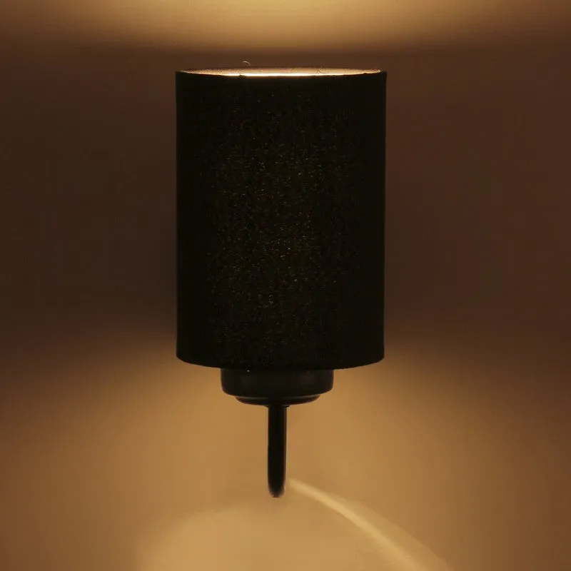 Lit black cylindrical wall lamp casting warm light on a dark wall