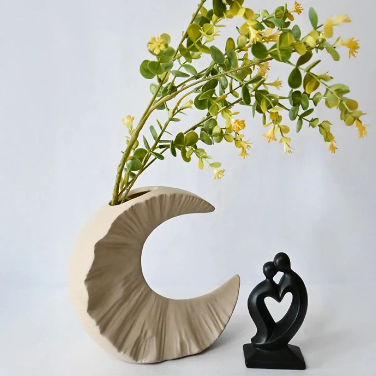 Beige half-moon vase with yellow stems beside a black figurine