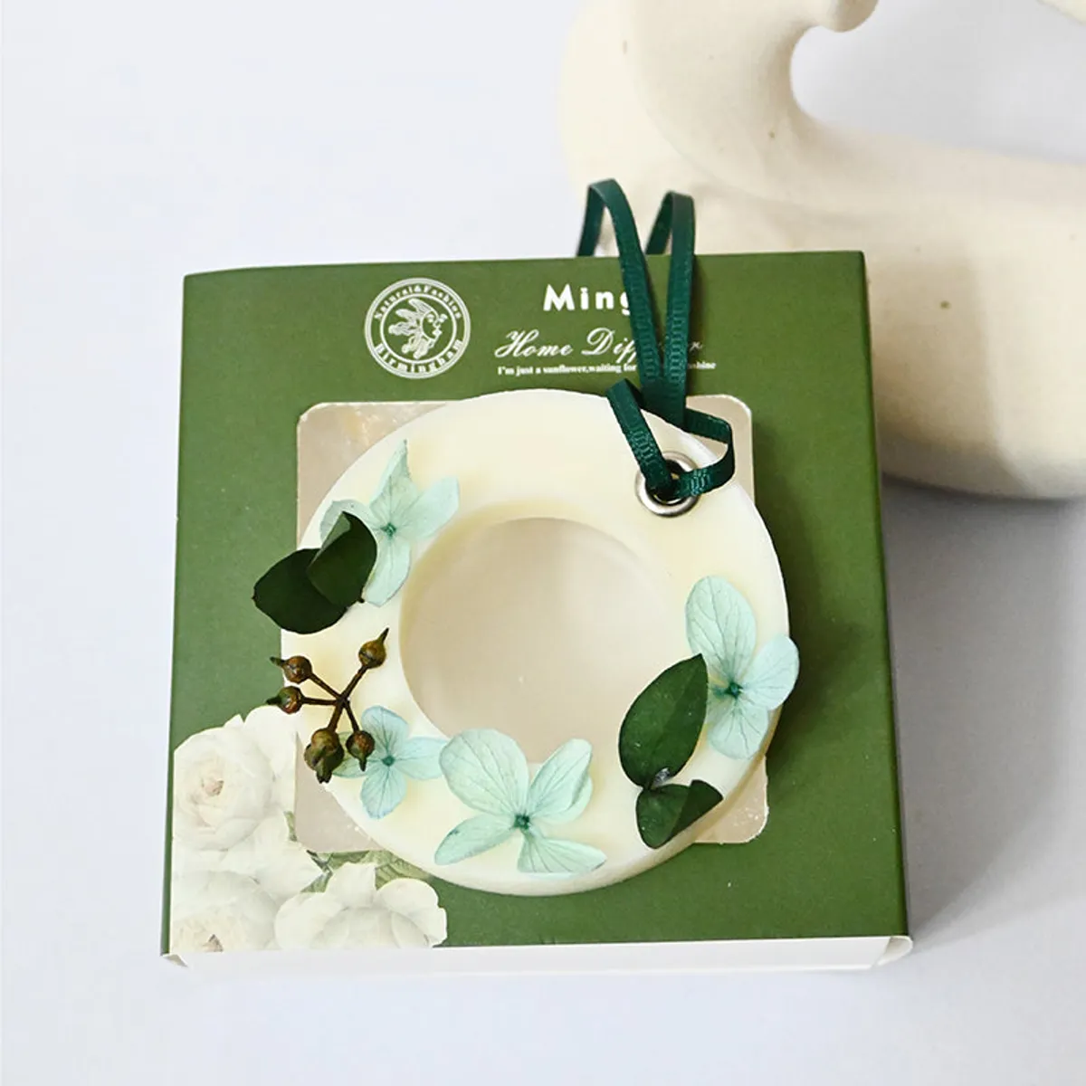 Round floral wax melt resting on a green product box