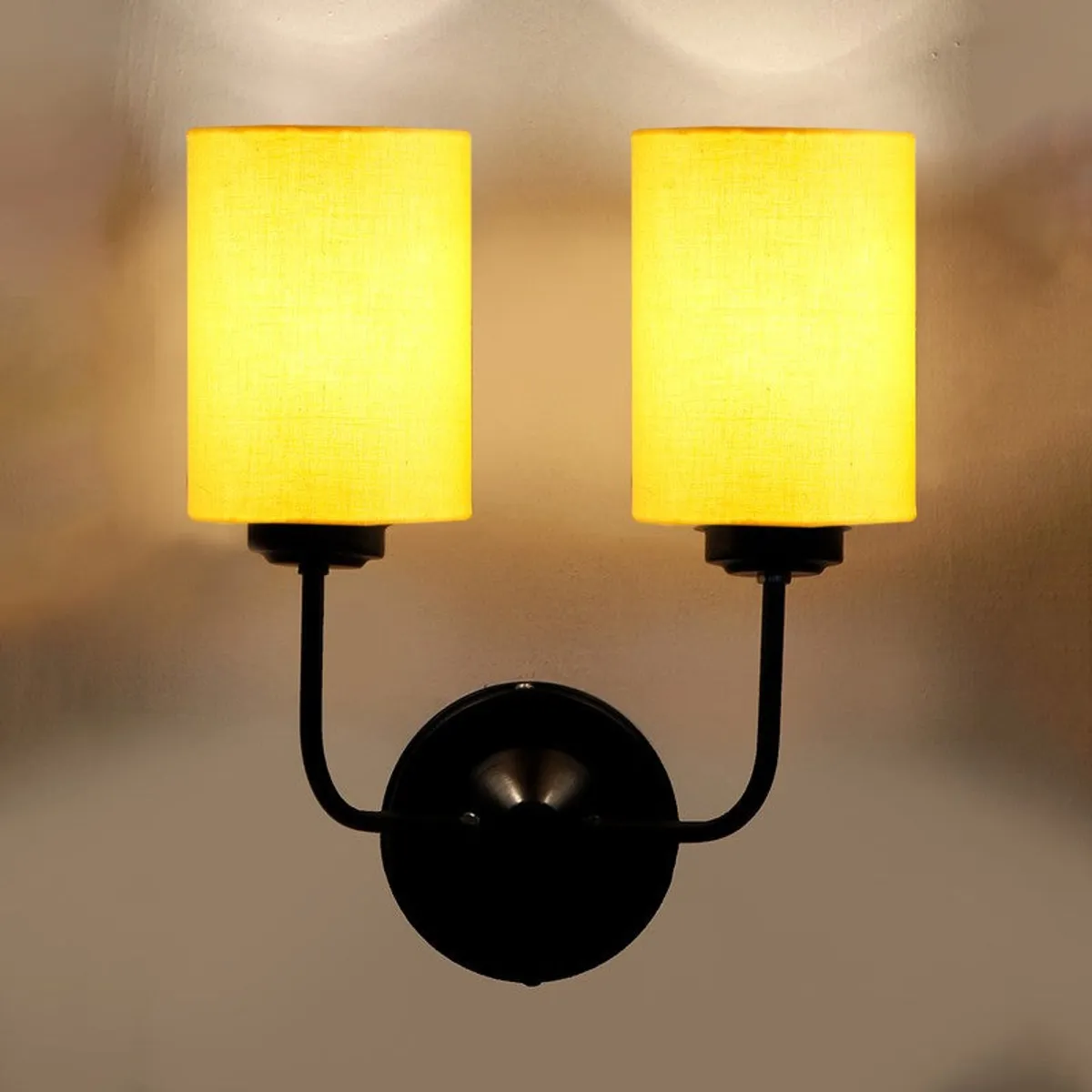 Close-up of lit yellow twin-shade wall lamp with black wall mount