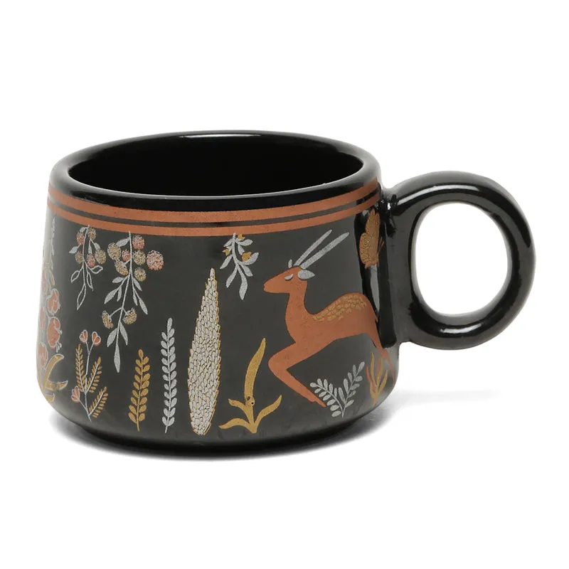 Close-up of a glossy black ceramic tea cup with a wildlife and botanical design