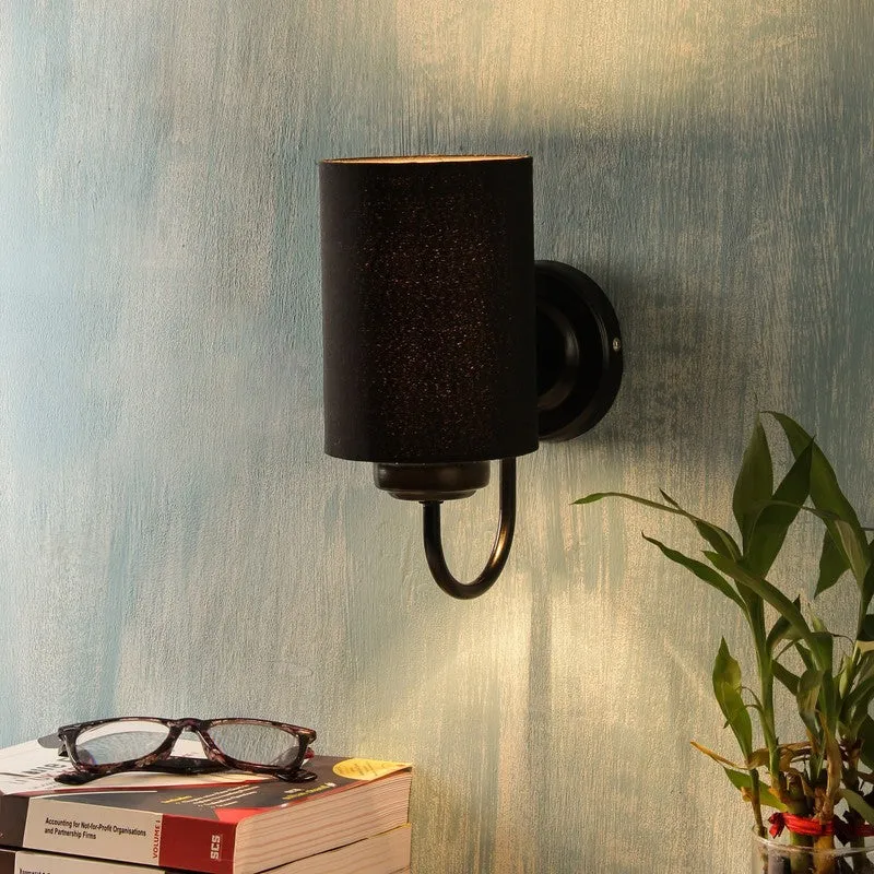 Black cylindrical wall lamp with round backplate mounted on a textured blue wall