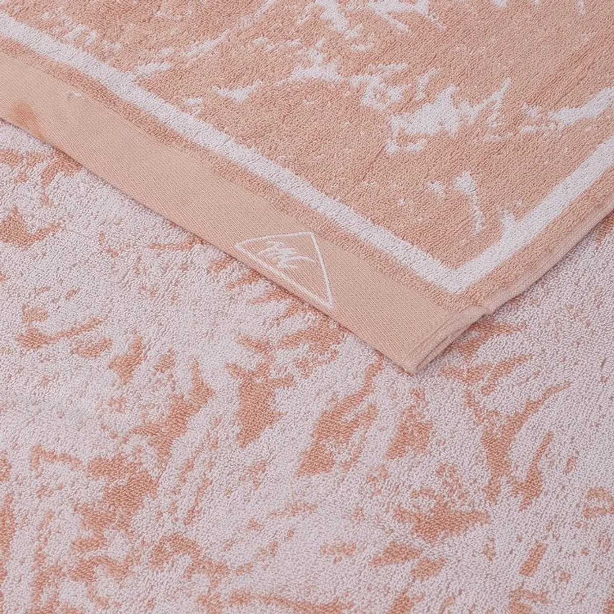 Close-up of peach and off-white floral towel fabric with a neat finished border