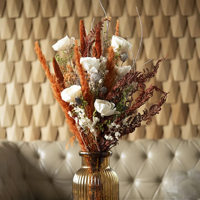 Dried bouquet with white flowers and rust-toned stems in an amber ribbed vase