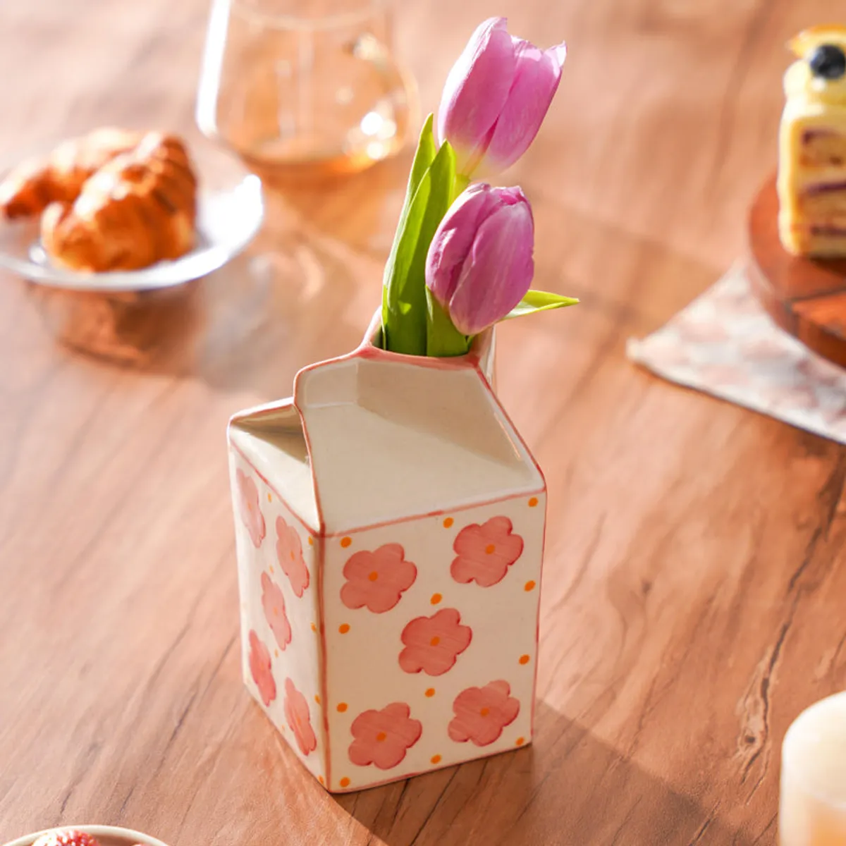 Floral carton-shaped vase holding pink tulips on a wooden table