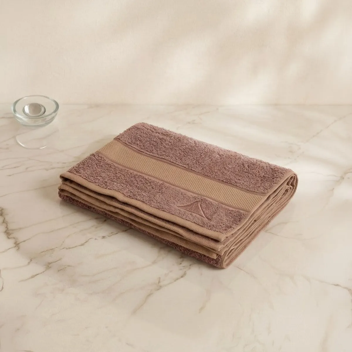 Folded camel-brown bath towel with contrasting bands on a marble surface