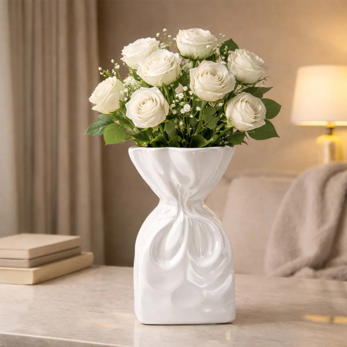 White sculptural vase holding white roses on a marble table in a softly lit room