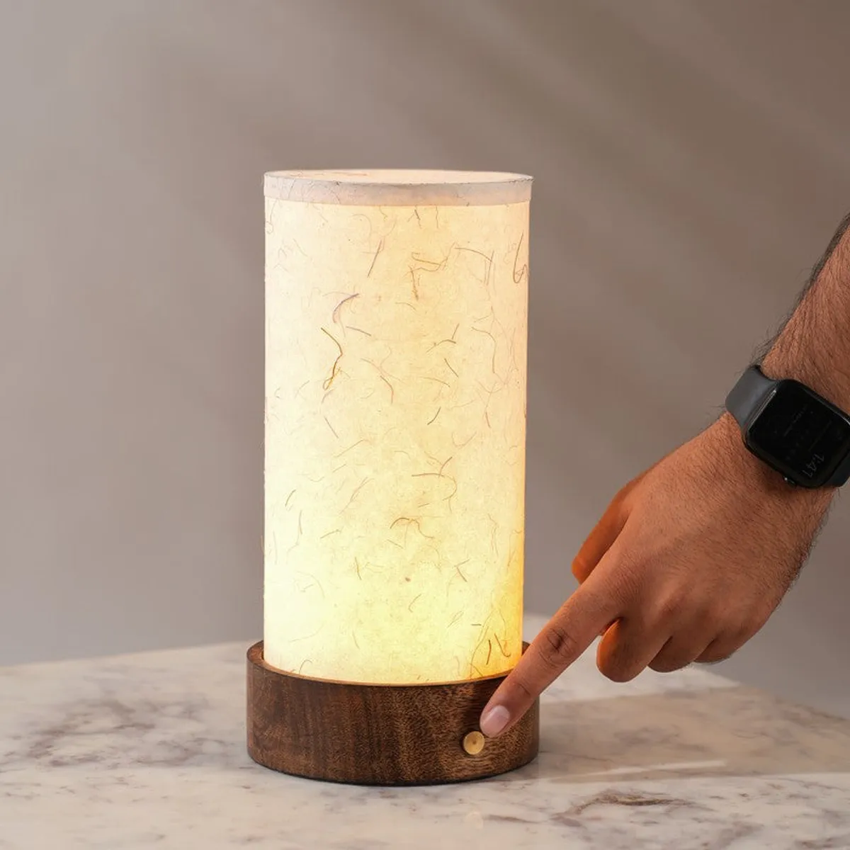 Hand pressing the button on the wooden base of the lit lamp