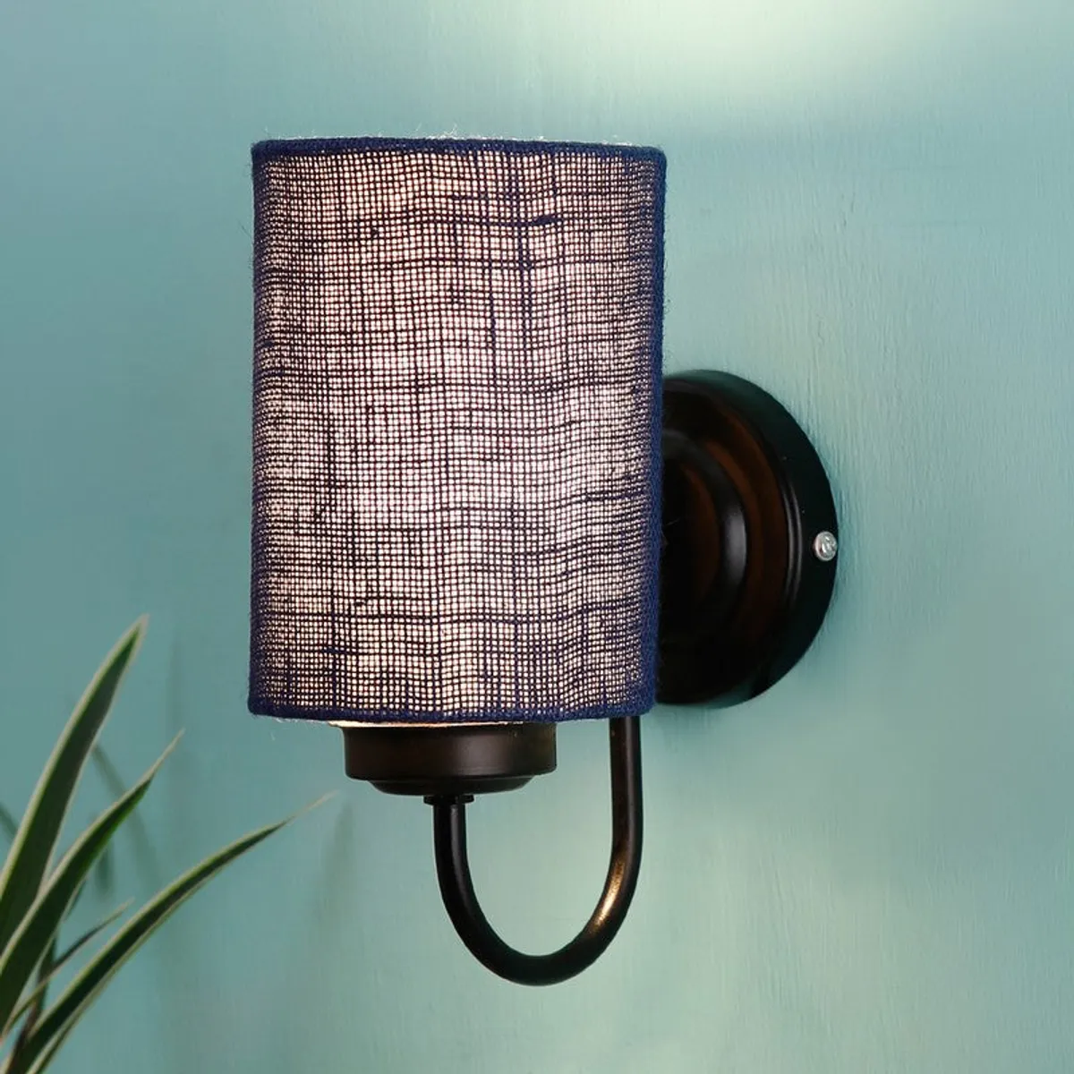 Close-up of blue cylindrical jute wall lamp with black iron base on blue wall