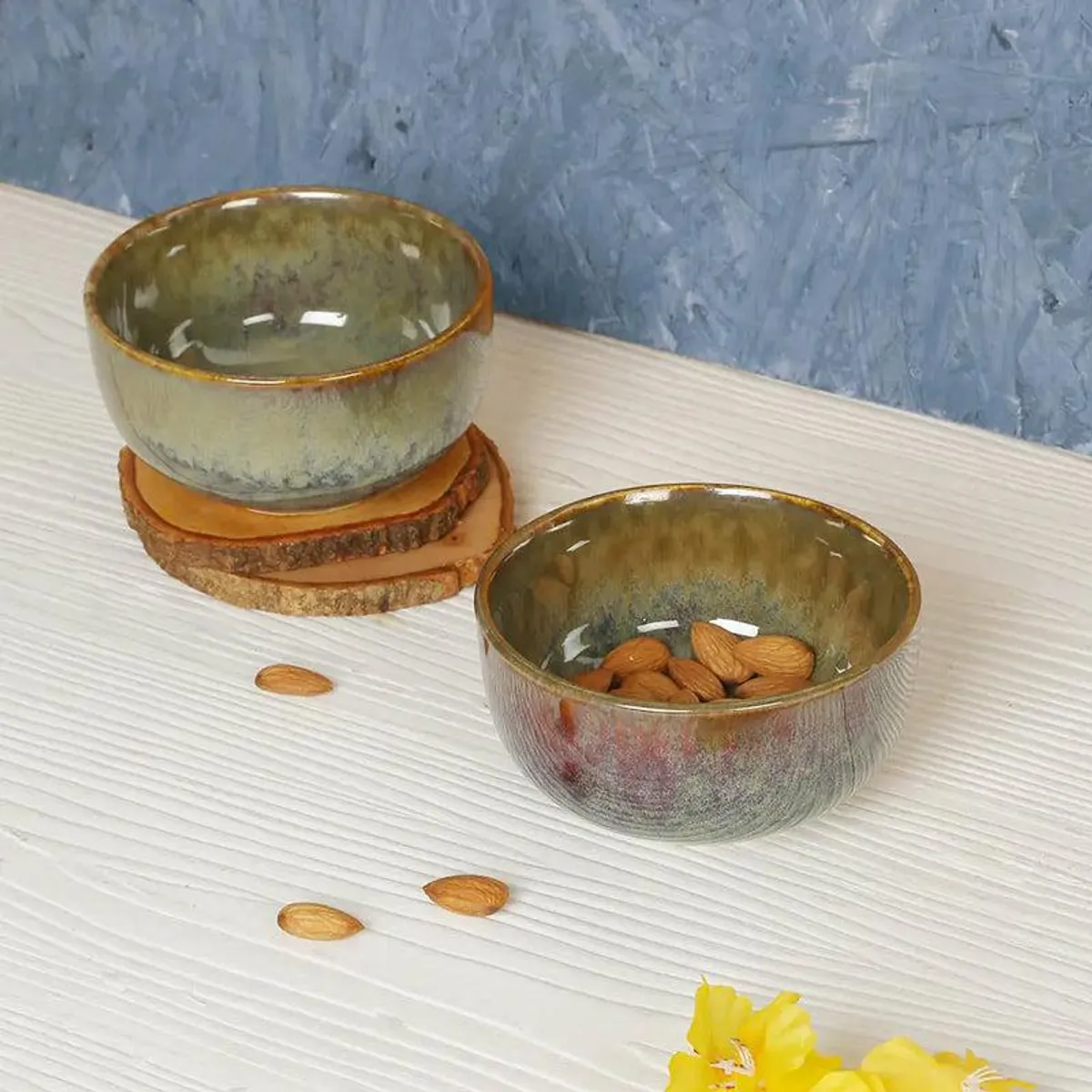 Glossy earthy green ceramic serving bowl styled with almonds and wooden coasters