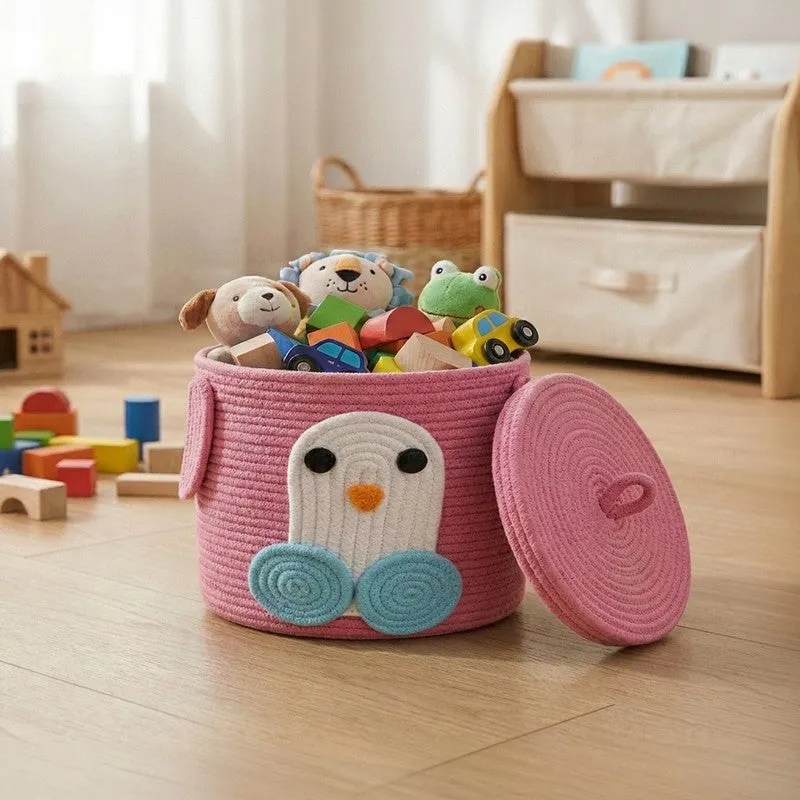 Pink cylindrical cotton storage basket with penguin motif and lid, filled with toys