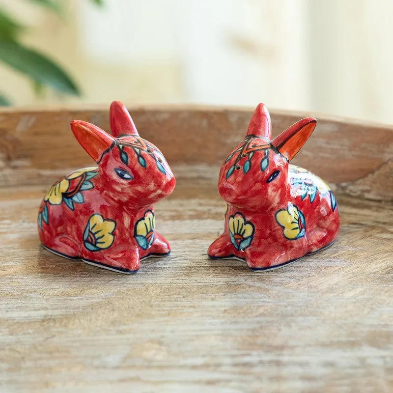 Pair of red rabbit-shaped ceramic salt and pepper shakers with floral motifs on a wooden surface