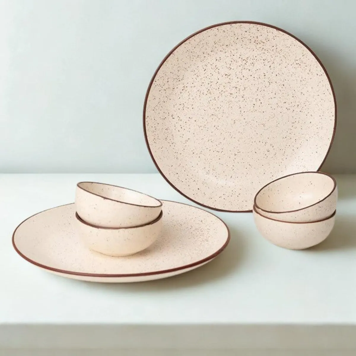 Beige speckled dinnerware with two plates and four bowls arranged against a light background.