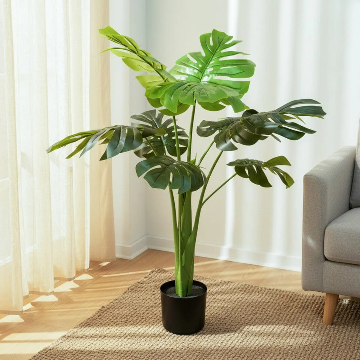 Artificial Monstera plant with layered green leaves in a black pot beside a sofa