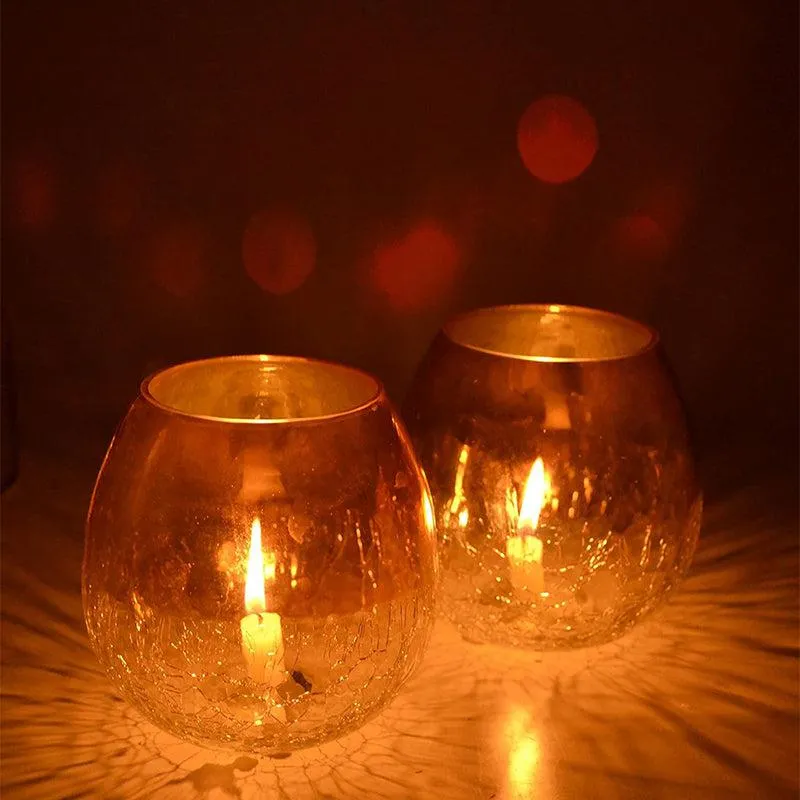 Two glowing golden glass tealight holders creating warm light on a surface