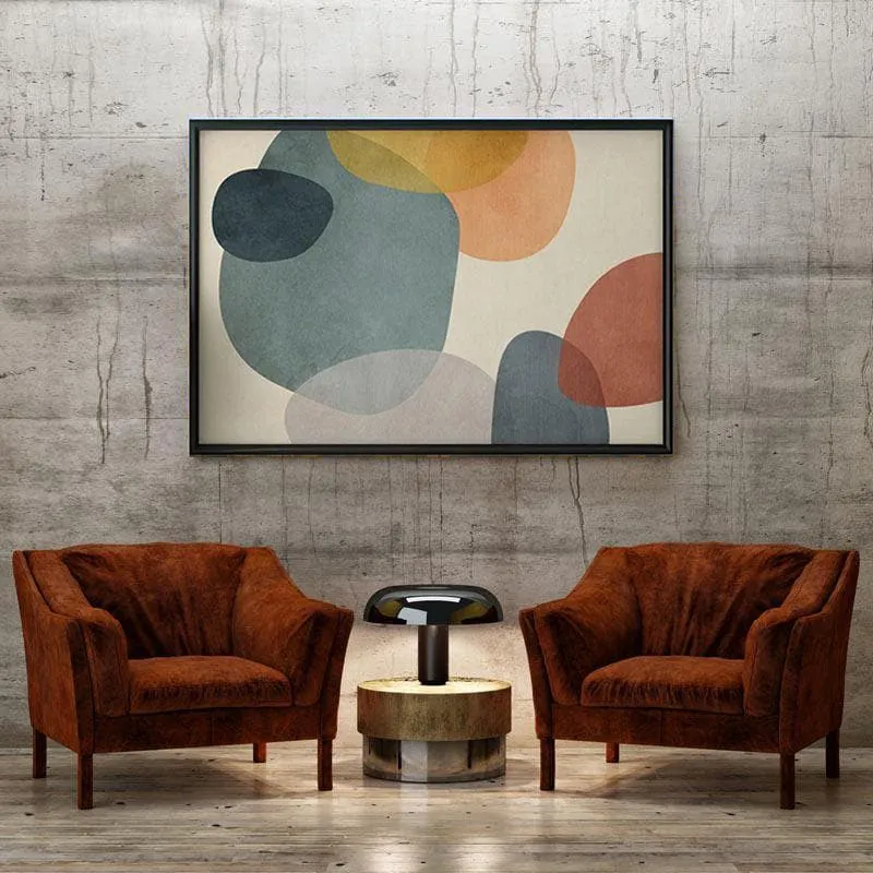 Black-framed abstract geometric painting displayed on a concrete wall between two brown armchairs