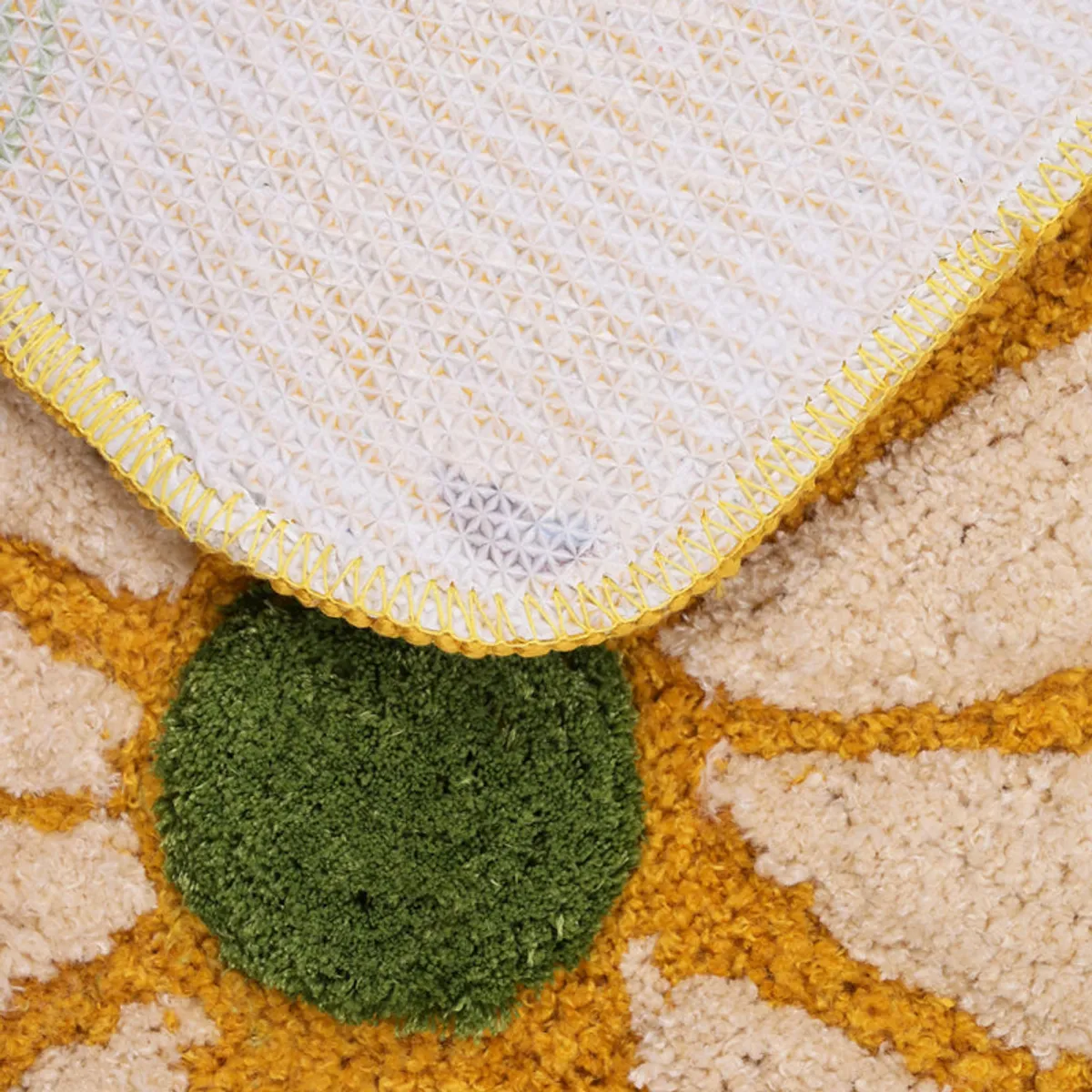 Close-up of the bathmat's underside with a pale textured backing and stitched yellow edge