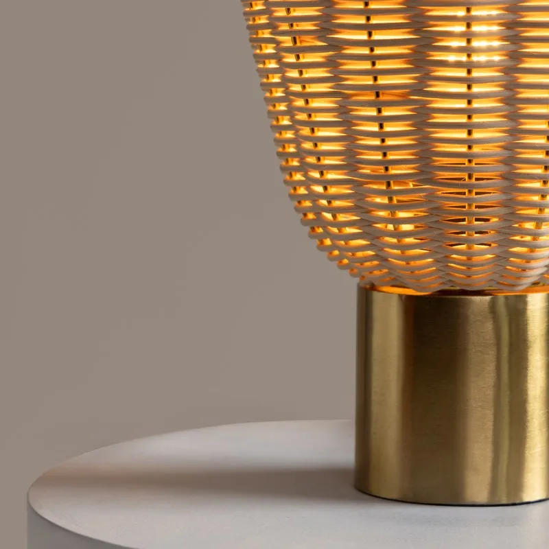 Close-up of the glowing rattan shade and gold metal base of a table lamp