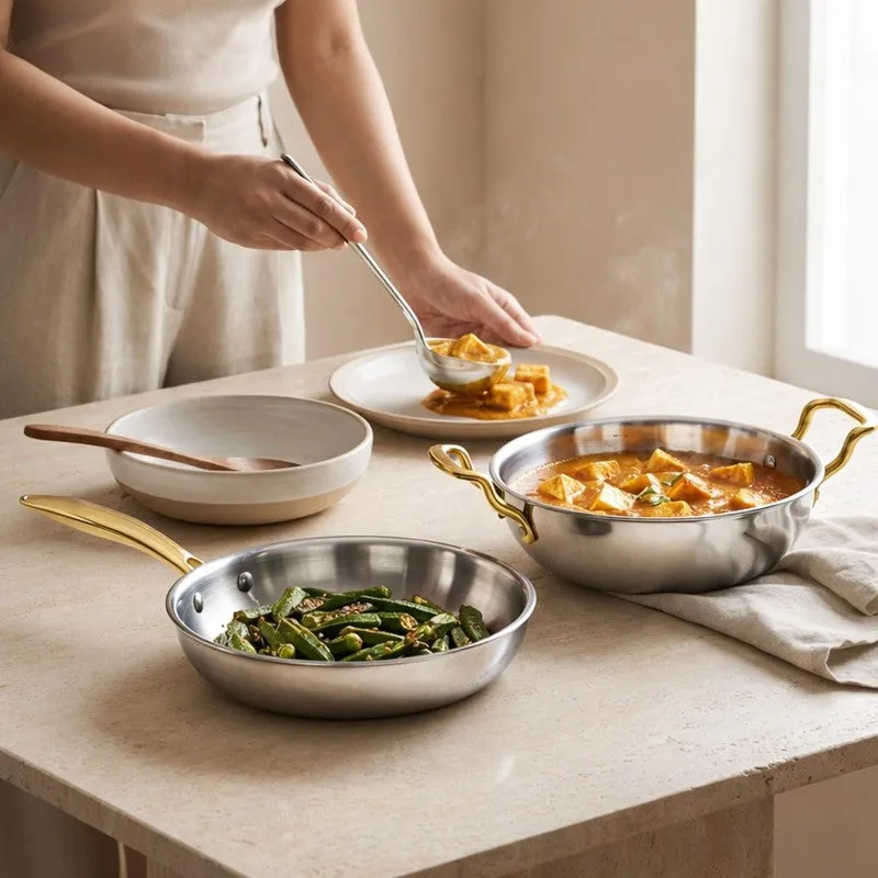 Silver frying pan and kadhai with gold handles styled on a dining counter