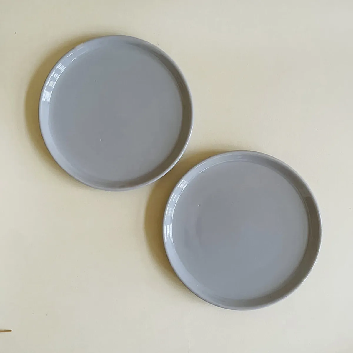 Two round grey ceramic plates arranged separately on a light surface.