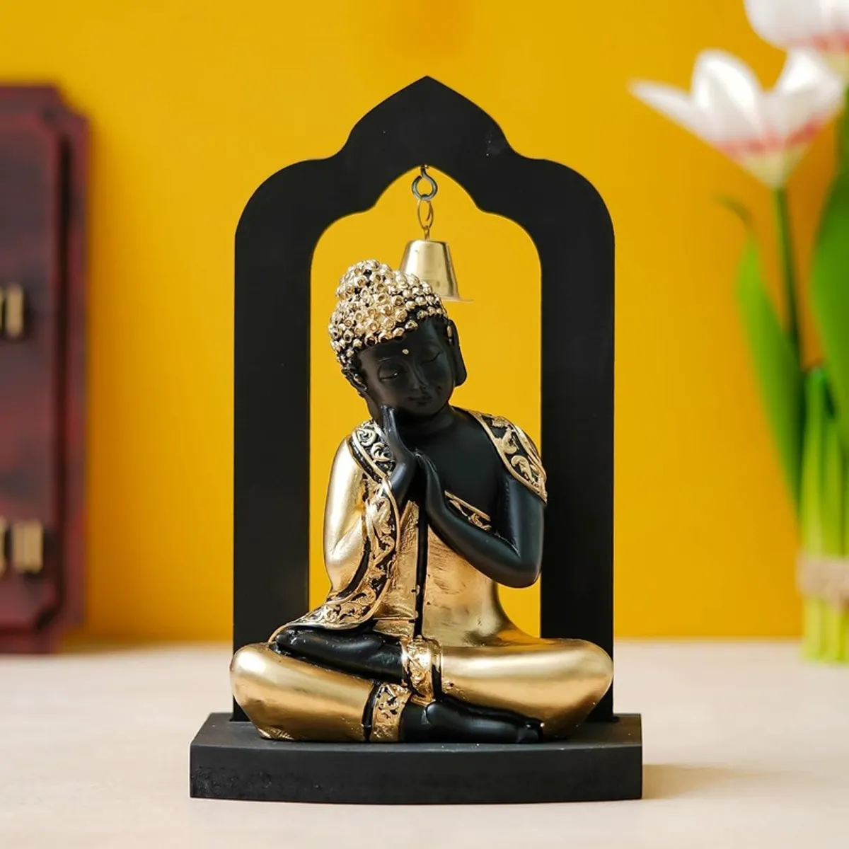 Front view of black and gold Buddha idol with hanging bell in wooden frame