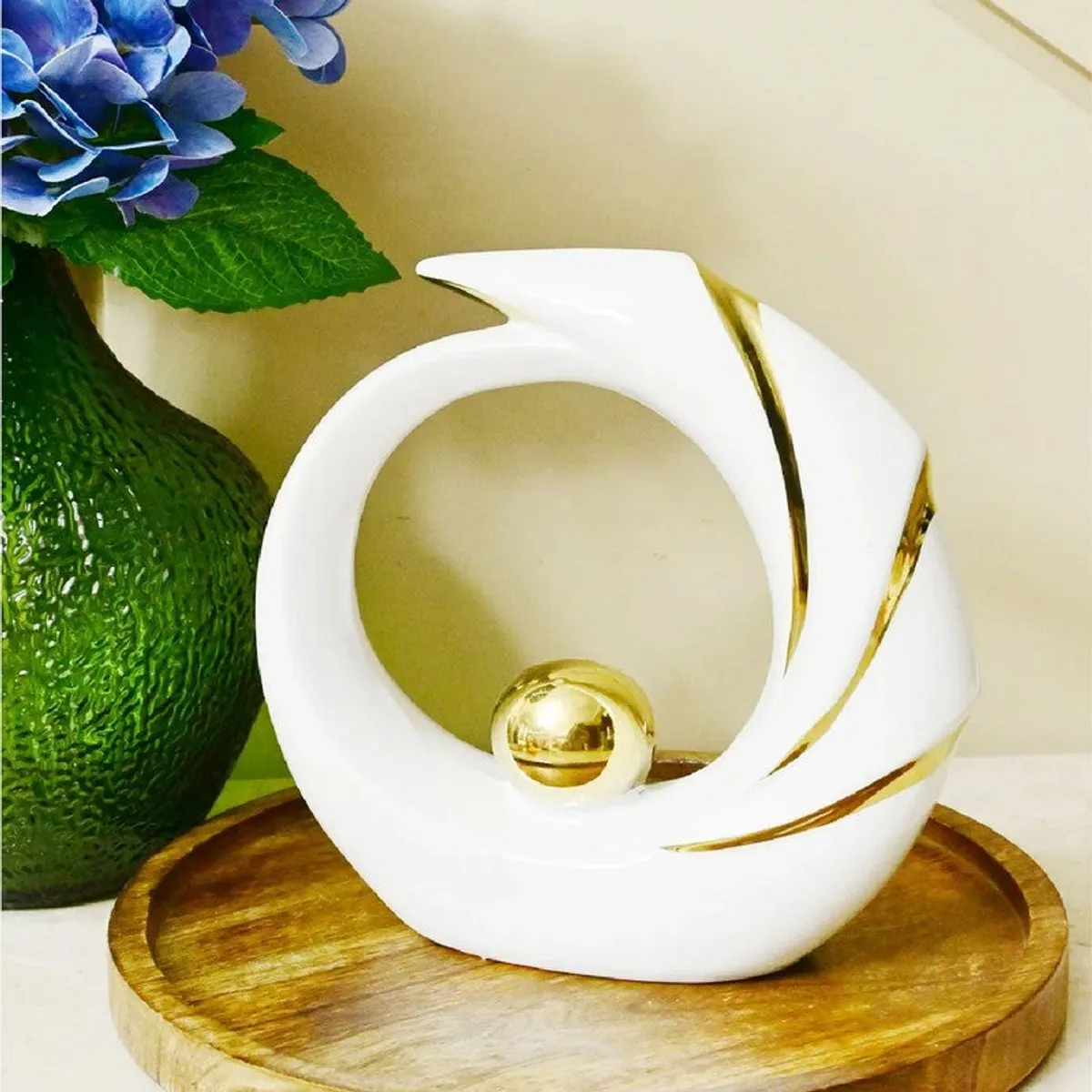 White sculptural showpiece with gold details on a wooden tray beside a green vase