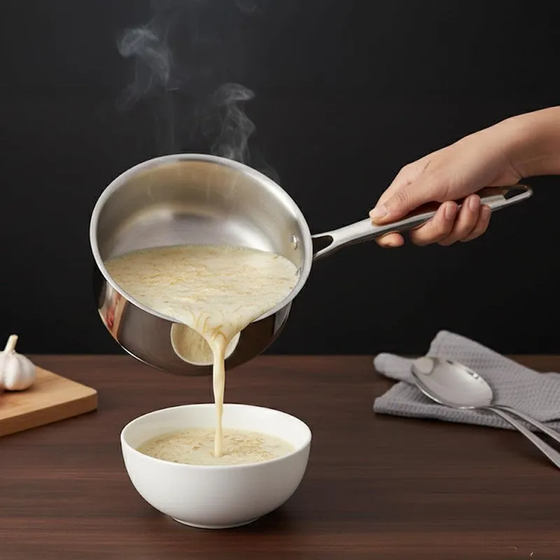 Hand pouring a creamy dish from a silver saucepan into a white bowl