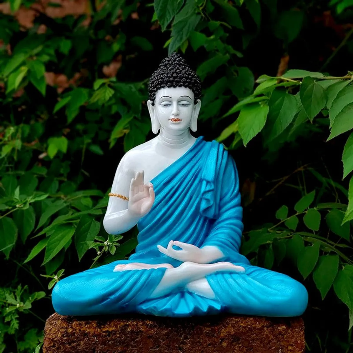 Blue and white seated Buddha idol displayed outdoors against green foliage