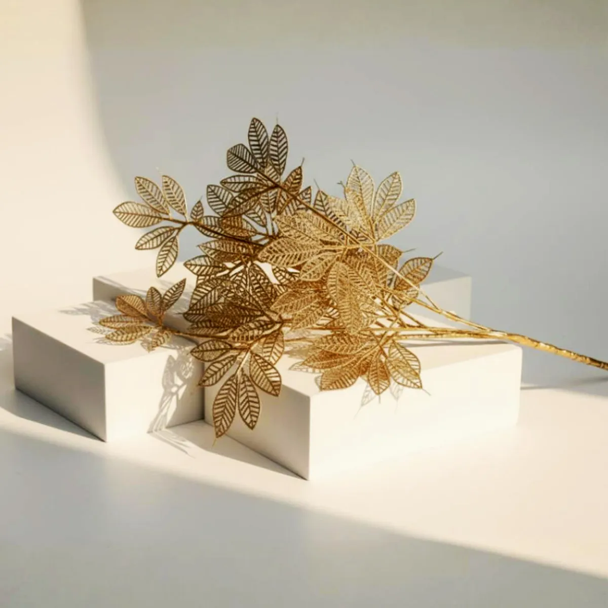 Golden artificial stems arranged in a wooden vase against a warm wall